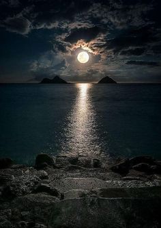 the full moon is setting over the ocean with rocks and water in front of it