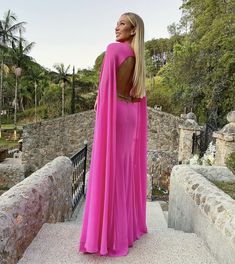 a woman in a long pink dress standing on a stone bridge looking off into the distance