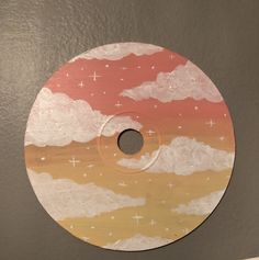 a painted disc with clouds and stars in the sky on it's side, sitting on a wall