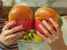 two hands hold up red bowls with hamburgers in them and they are holding each other