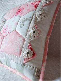 a pink and white pillow with flower appliqued on the front, sitting on a bed