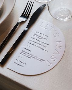 a place setting with silverware and menus on a white table cloth covered table