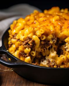 a skillet filled with macaroni and cheese on top of a wooden table