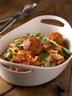 a white bowl filled with spaghetti and meatballs on top of a wooden table next to a fork