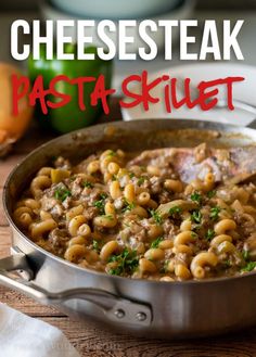 a skillet filled with pasta and meat on top of a wooden table next to vegetables