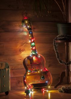 an electric guitar with christmas lights on it is sitting in front of a wooden wall