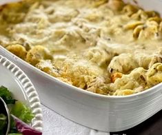 a casserole dish with meat and vegetables in it on a table next to a salad