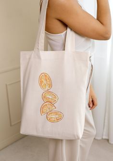 "This cute orange canvas tote bag is ready for a trip to the farmers market, or to carry your book to your favorite coffee shop. This tote bag is versatile as a book bag, grocery bag, or errand tote. The design of the hand-drawn orange on the front makes this bag a perfect statement piece!  Details: - One size: 15\" x 16\"  - 20\" handle length  - 100% cotton canvas tote - Lightweight and compact - Print is on one side, the other side is blank  - The reinforced handle stitching creates a reliable bag for practicality and durability Care instructions:  - Pretreat visible stains with stain remover.  - Mix warm water with laundry detergent and clean the bag with a terry washcloth or a soft bristle brush.  - Let the bag air dry." Orange Canvas Bag For Daily Use, Casual Orange Cotton Canvas Bag, Orange Cotton Canvas Bag For Everyday Use, Orange Canvas Tote Bag, Orange Cotton Shopping Bag, Eco-friendly Orange Canvas Bag For Everyday Use, Orange Cotton Canvas Tote Bag, Orange Tote Bags, Fruit Illustration