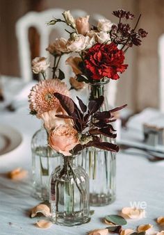 two vases filled with flowers sitting on top of a white tablecloth covered table