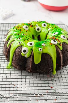 a chocolate cake with green icing and eyes on it's face is sitting on a cooling rack