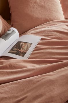 an open book sitting on top of a bed covered in pink sheets and pillow cases