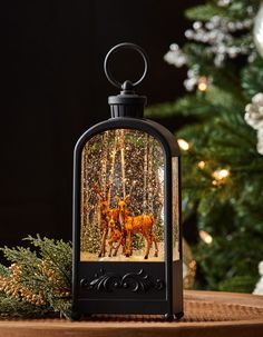 a lantern with two deers in it sitting on a table next to a christmas tree