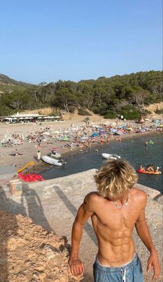 a man standing on top of a cliff next to a beach filled with lots of people