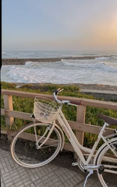 a white bicycle parked next to a wooden fence near the ocean with waves in the background