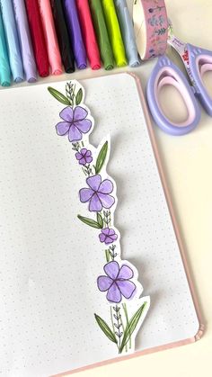 an open notebook with flowers and scissors next to it on a table filled with crayons