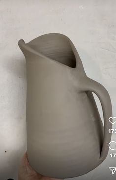 a hand holding a gray ceramic pitcher on a white wall