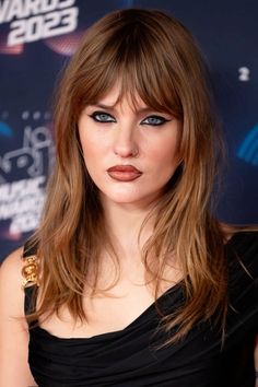 a close up of a person with long hair and blue eyeshadow wearing a black dress