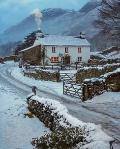 a white house sitting on the side of a snow covered road next to a stone wall