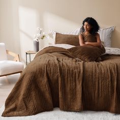 a woman sitting on top of a bed under a brown blanket