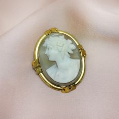 "A beautiful and romantic Art Nouveau or Edwardian natural, hand-carved shell cameo brooch/pendant, circa 1900-1910. The cameo depicts an ancient Greek motif - a young woman with a Hellenic tiara, flowers in her hair and locks of hair.   Incased in a smooth oval gold filled or rolled gold frame with leaf ornaments on all sides.  The cameo is white with touches of pink on the neck, hair bun and robe, carved from a single piece of shell with a taupe pinkish background. Perfect gift for a young gir Antique Carved Brooches For Weddings, Victorian Style Cameo Brooch For Weddings, Victorian Cameo Brooch For Wedding, Antique Cameo Brooches For Wedding, Art Nouveau Cabochon Brooches For Weddings, Art Nouveau Cabochon Wedding Brooches, Antique White Cameo Brooch, Antique Oval Carved Brooches, White Oval Cameo Brooches