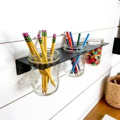 three jars with pencils are hanging on the wall