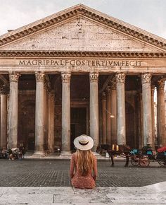 a woman sitting on the ground in front of an old building with columns and pillars