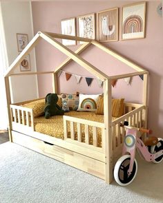 a child's bed with a pink bicycle in front of it and pictures on the wall