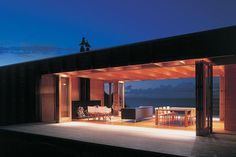 an outdoor living area is lit up at night with the ocean in the back ground