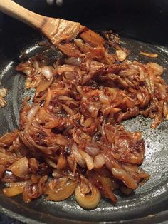 onions being cooked in a skillet with a wooden spoon