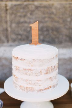 a white cake sitting on top of a table with a wooden number one on it