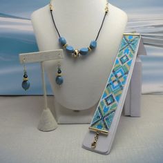 The good look of turquoise and gold is what makes this set so becoming. This bracelet/necklace/earrings set has a geometric design of diamond shapes. They are handmade with care using a bead loom to make the bracelet. Delica beads were used giving the bracelet a more polished and uniform look. The bead colors are silver lined teal, matte cyan turquoise blue, chrysoprase (light green), butter rum and white. The bracelet's pattern has a diamond shaped center with four diamond shapes inside and chevrons on the outside with a teal X shape. The ends have basically the same, diamonds with a teal X shape adding an arrow shape. It has gold plated tube ends and an extension chain of 1 1/2 inches for sizing... or to loosen the fit, simply hook into the chain. From the lobster claw clasp to the ring Royal Blue Jewelry, Green Butter, Butter Rum, Blue Jewelry Set, Gift Sets For Her, Turquoise And Gold, Glass Beads Jewelry, Ear Earrings, Christmas Bracelet