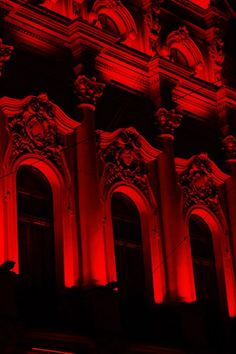 a building with red lights on it's side and the windows lit up at night