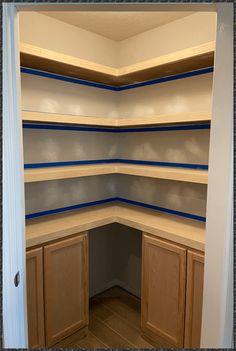 an empty pantry with wooden cabinets and blue tape on the shelves in it's corner