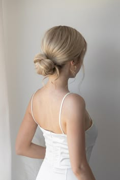 a woman in a white dress is looking down at her hair and wearing an updo