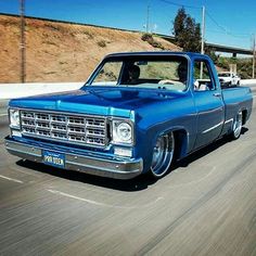 an old blue truck driving down the road