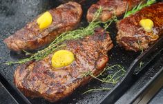 some steaks are cooking on a grill with lemon slices and green garnish