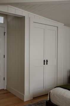 an empty bedroom with white closets and wood flooring on the walls, along with a bed