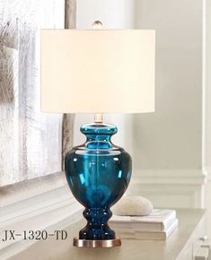 a blue glass lamp sitting on top of a table next to a white book and a window