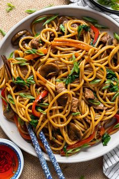 a white bowl filled with noodles and meat on top of a table next to chopsticks