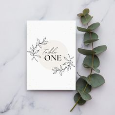 a card with the words, one on it next to eucalyptus leaves and greenery