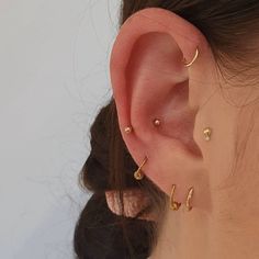 a woman wearing three different ear piercings on her left ear and the other one is gold