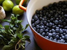 blueberries and green apples are in a pot next to other fruit on the table