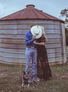 a man and woman standing next to each other in front of a metal silo