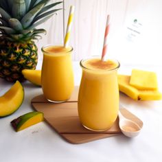 two glasses filled with orange juice next to sliced pineapple