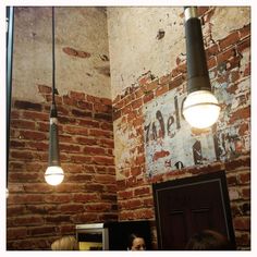 three people standing in front of a brick wall with two lights hanging from the ceiling