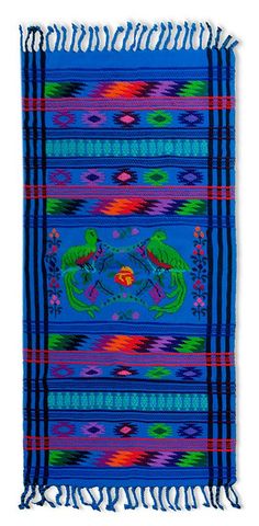 a blue blanket with colorful designs and fringes on the edges, in front of a white background