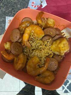 a person holding up a plate of food with shrimp, sausage and noodles on it