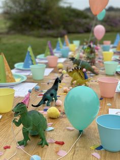 a table topped with balloons and plastic dinosaurs next to small cups filled with confetti