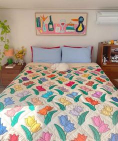 a bed with colorful quilts and pillows in a small room next to a dresser