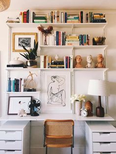 a white desk topped with lots of books next to a wall mounted shelf filled with books